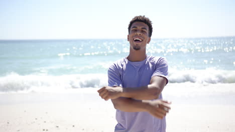 A-young-biracial-man-stretches-his-arms-on-a-sunny-beach-with-copy-space