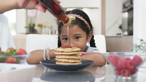 A-biracial-girl-with-dark-hair-smiles-as-syrup-is-poured-on-her-pancakes