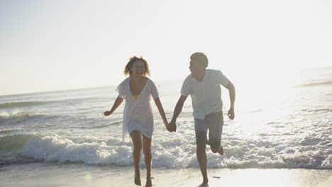Biracial-couple-enjoys-a-playful-run-along-the-beach-at-sunset