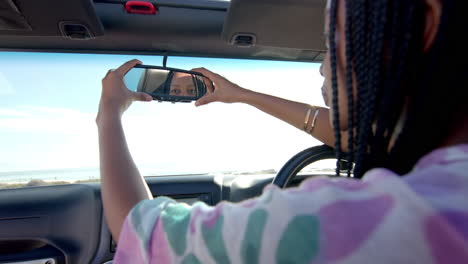 Young-African-American-woman-adjusts-the-rearview-mirror-in-her-car-on-a-road-trip