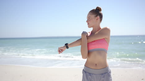 Young-Caucasian-woman-stretching-her-arm-on-a-sunny-beach,-with-copy-space