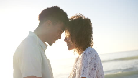 Biracial-couple-shares-a-tender-moment,-foreheads-touching-at-the-beach-during-sunset