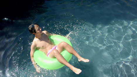 Teenage-Asian-boy-relaxes-on-a-pool-float,-with-copy-space