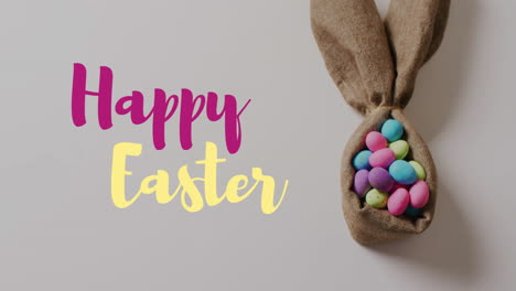 Animation-of-happy-easter-text-over-colourful-easter-eggs-in-cloth-on-grey-background