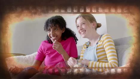 Animation-of-film-frame-over-two-happy-diverse-teenage-girls-watching-movie-with-popcorn-at-home