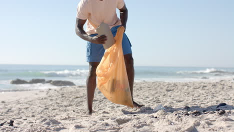 A-young-African-American-man-cleans-up-a-beach,-with-copy-space