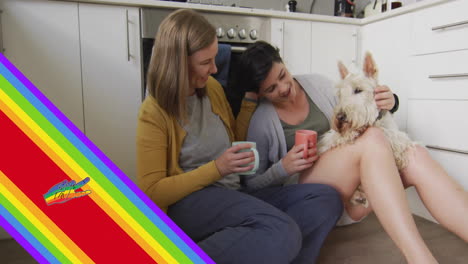 Animation-of-pride-rainbow-stripes-and-hand-over-caucasian-lesbian-couple-in-kitchen-with-pet-dog