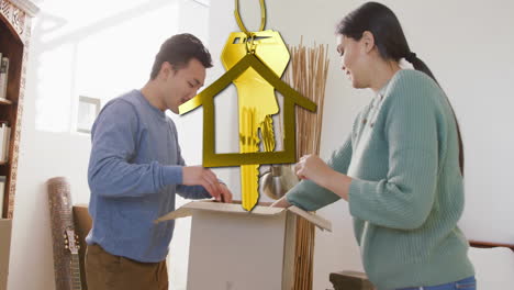 Animation-of-gold-house-key-and-key-fob-over-biracial-couple-unpacking-boxes-moving-in-new-home
