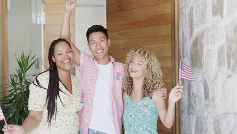 Waving-American-flags,-a-young-Asian-man-flanked-by-young-biracial-women,-all-smiling-with-'I-Voted'