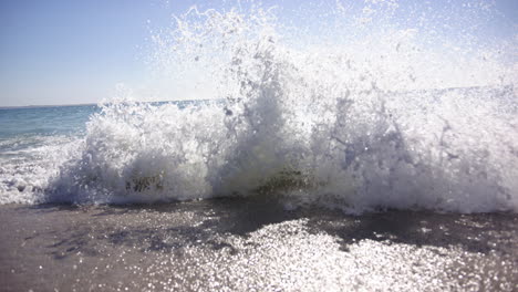 A-wave-crashes-onto-the-shore,-creating-a-dynamic-spray-of-water-with-copy-space
