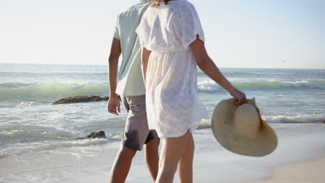 Biracial-couple-stands-on-a-sandy-beach,-facing-the-sea