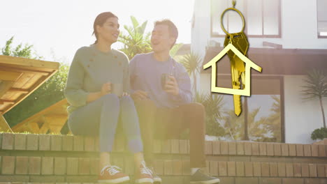 Animation-of-gold-house-key-and-key-fob-over-diverse-couple-drinking-tea-at-new-home
