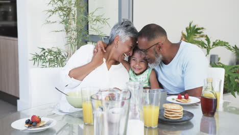 Biracial-grandparents-enjoy-breakfast-with-their-young-granddaughter,-sharing-a-loving-moment