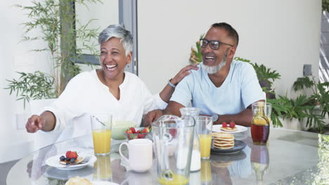 Biracial-couple-enjoys-a-hearty-breakfast,-sharing-a-laugh-together