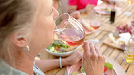 Senior-biracial-woman-enjoys-a-glass-of-wine-at-an-outdoor-dining-table