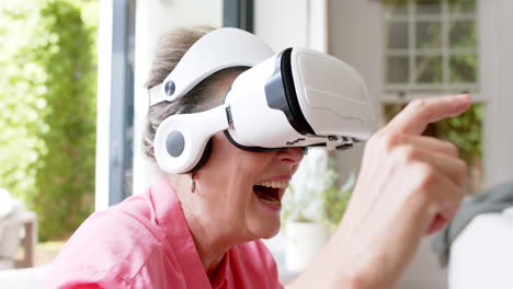 Senior-Caucasian-woman-is-engaged-with-a-virtual-reality-headset,-smiling-broadly