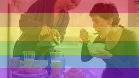 Animation-of-pride-rainbow-stripes-over-happy-caucasian-lesbian-couple-having-coffee-and-breakfast