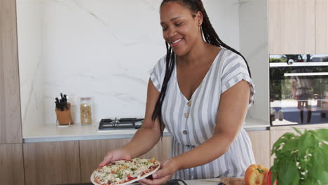 Young-biracial-woman-prepares-a-meal,-including-making-pizza,-in-a-modern-home-kitchen