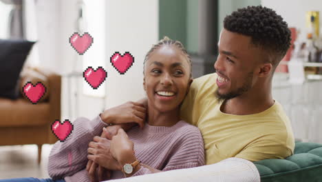 Animation-of-hearts-over-happy-diverse-couple-on-sofa-at-home