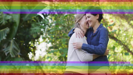 Animation-of-pride-rainbow-stripes-over-happy-caucasian-lesbian-couple-embracing-in-garden