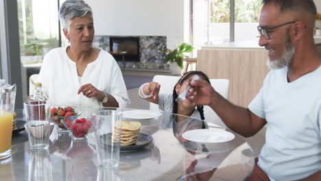 Biracial-family-enjoys-breakfast,-with-a-child-reaching-for-food
