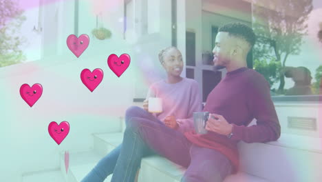 Animation-of-hearts-over-happy-diverse-couple-drinking-tea-at-home