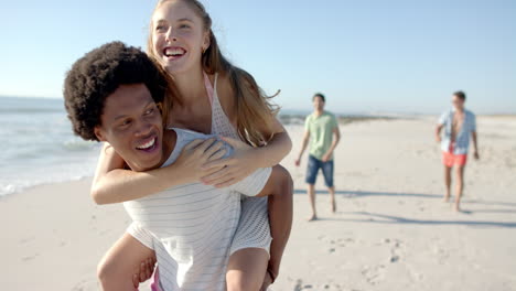 Young-Caucasian-woman-enjoys-a-piggyback-ride-from-an-African-American-man-on-the-beach