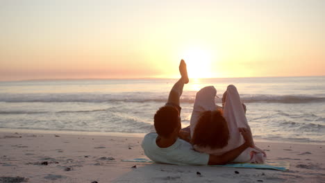 Biracial-couple-relaxes-on-the-beach-at-sunset,-legs-playfully-raised-in-the-air-with-copy-space