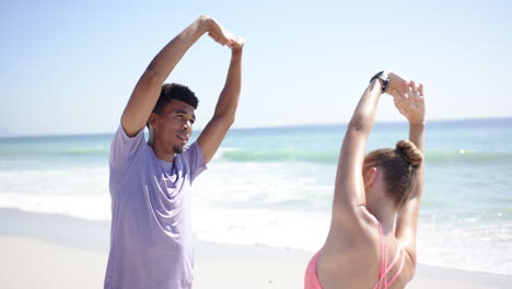 Young-biracial-man-and-Caucasian-woman-stretch-on-a-sunny-beach