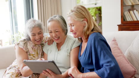 Senior-biracial-woman,-Asian-woman,-and-Caucasian-woman-laughing-and-using-a-tablet-at-home