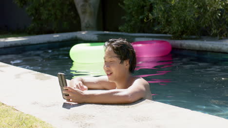 Teenage-Asian-boy-enjoys-a-sunny-day-by-the-pool-using-a-smartphone