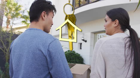 Animation-of-gold-house-key-and-key-fob-over-happy-biracial-couple-by-house