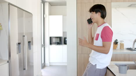 Teenage-Asian-boy-enjoys-a-beverage-in-a-modern-kitchen,-with-copy-space
