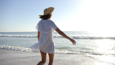 A-young-biracial-woman-enjoys-a-walk-along-the-shoreline,-her-white-dress-flowing-in-the-breeze