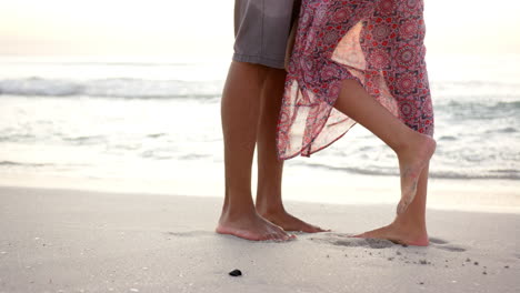 Barefoot-couple-stands-close-on-a-sandy-beach,-with-a-woman-in-a-patterned-dress