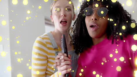 Animation-of-yellow-lights-over-two-diverse-teenage-girls-miming-singing-with-tv-remote-control