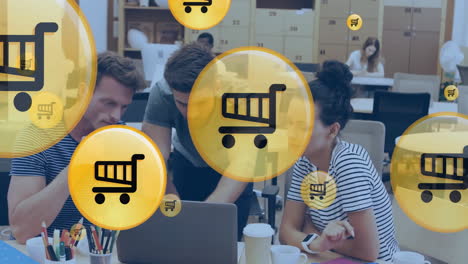 Animation-of-shopping-cart-icon-over-diverse-colleagues-discussing-work-in-office