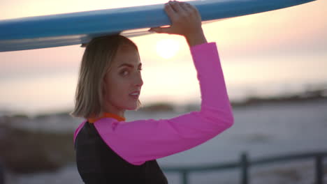 Young-Caucasian-woman-carries-a-surfboard-at-sunset