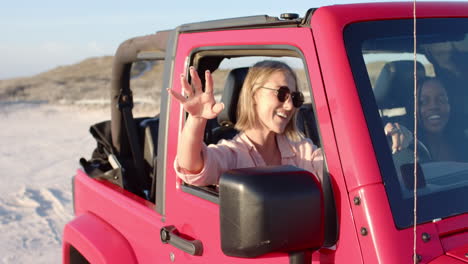 Young-Caucasian-woman-and-African-American-woman-enjoy-a-sunny-day-in-a-pink-jeep-on-a-road-trip,-wi