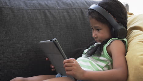 Biracial-girl-with-dark-hair-enjoys-a-tablet-while-wearing-headphones
