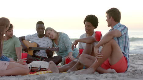 Diverse-friends-enjoy-music-on-the-beach-at-sunset