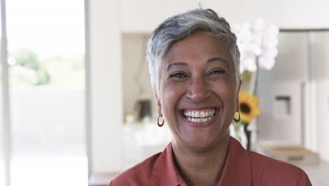 Biracial-woman-with-short-gray-hair-smiles-warmly,-wearing-a-red-shirt-and-gold-earrings