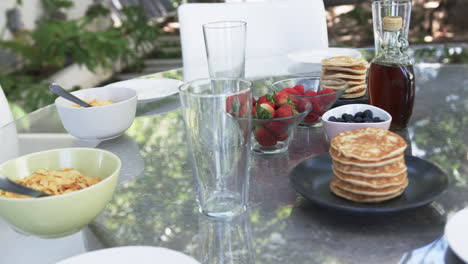A-breakfast-spread-features-pancakes,-strawberries,-blueberries,-and-cereal-on-an-outdoor-table