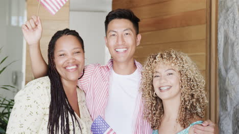 Young-Asian-man-and-two-young-biracial-women-pose-cheerfully-with-waving-American-flags