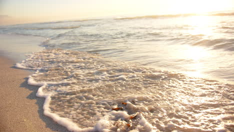Sanfte-Wellen-Spülen-Bei-Sonnenuntergang-über-Den-Sandstrand,-Mit-Einem-Warmen-Schein-Am-Horizont,-Mit-Kopierraum