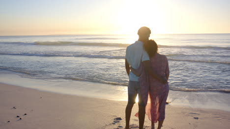 Biracial-couple-embraces,-silhouetted-against-a-beach-sunset-with-copy-space