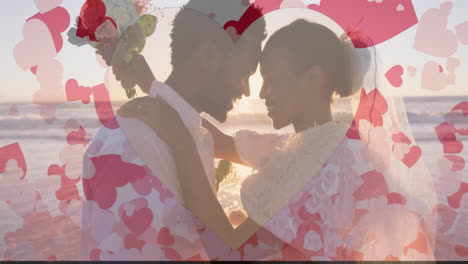 Animation-of-hearts-over-happy-diverse-just-married-couple-embracing-on-beach-by-sea