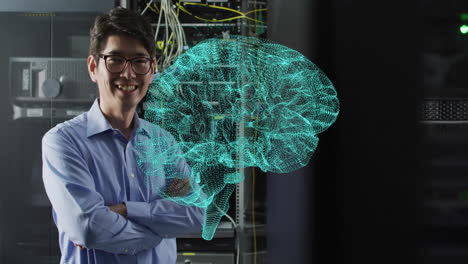 Animation-of-glowing-brain-network-over-smiling-asian-male-technician-in-dark-server-room