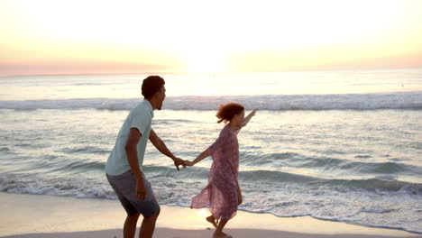 Biracial-couple-enjoys-a-playful-moment-on-the-beach-at-sunset