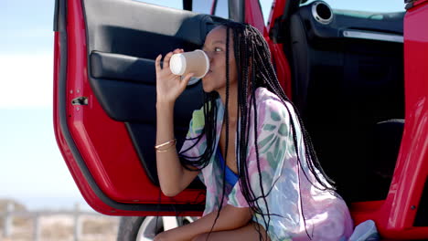 Young-African-American-woman-enjoys-a-drink-outdoors-on-a-road-trip